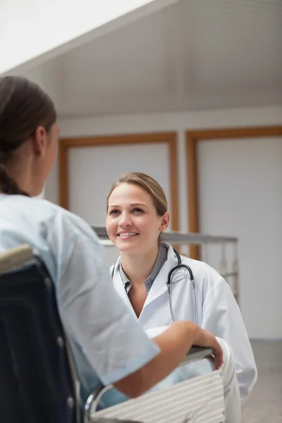 Smiling doctor squatting next to a patient on a wheelchair Stock Image