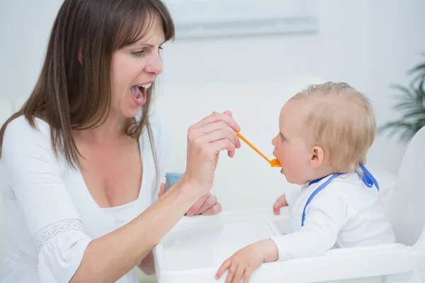 Mother feeding a baby while opening her mouth Stock Picture