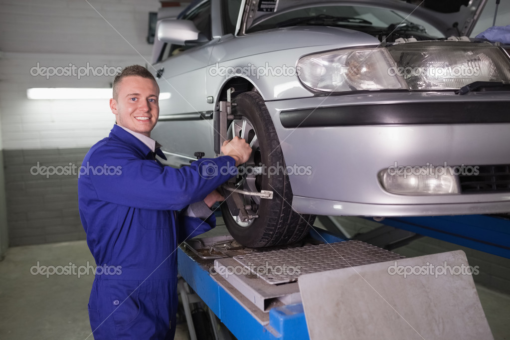 Uśmiechający się mechanik stojący a naprawy samochodu koło