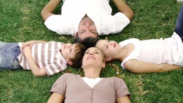 Famiglia sorridente sdraiata in un parco con le teste unite — Video Stock