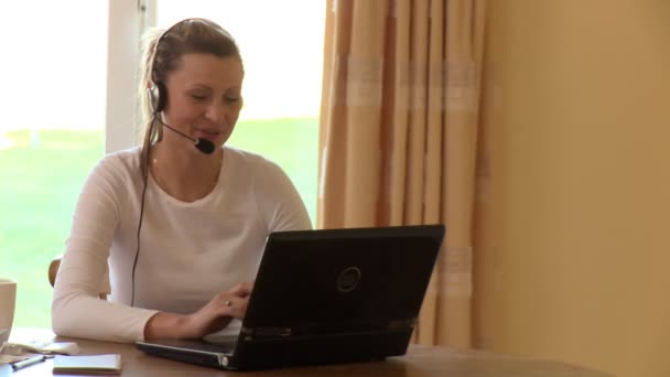 Χαρούμενα γυναίκα με ακουστικό σχετικά με τη χρήση ενός φορητού υπολογιστή — Αρχείο Βίντεο