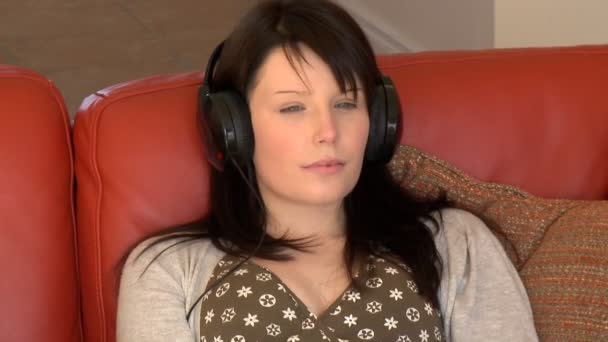 Расслабленная женщина сидит на диване и слушает музыку — стоковое видео