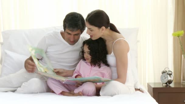 Eltern lesen mit ihrer Tochter ein Buch im Bett — Stockvideo