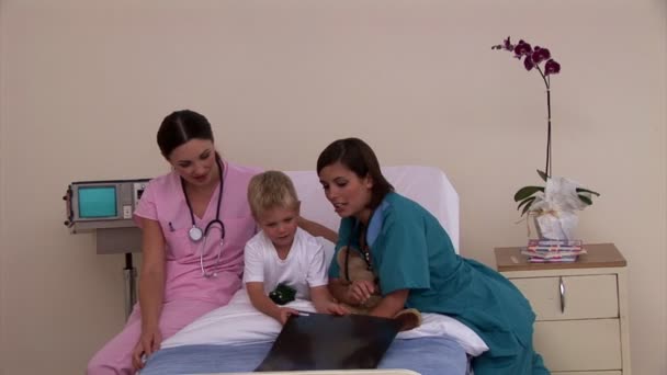 Twee positieve verpleegkundigen x-ray tonen aan een kleine jongen — Stockvideo