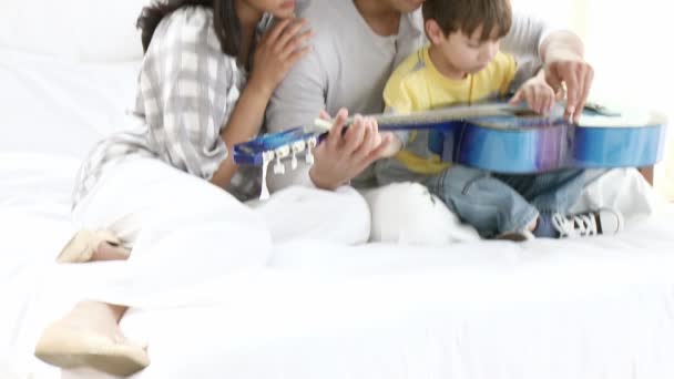 Młodzi rodzice i synek gra na gitarze na kanapie w domu — Wideo stockowe