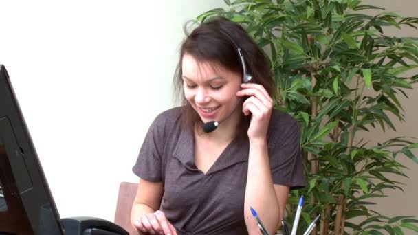 Mujer sonriente con auriculares en el trabajo en un ordenador — Vídeo de stock