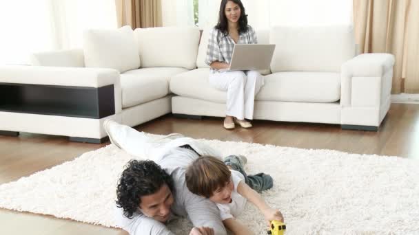 Папа и маленький мальчик играют в видеоигры, а мама использует ноутбук — стоковое видео