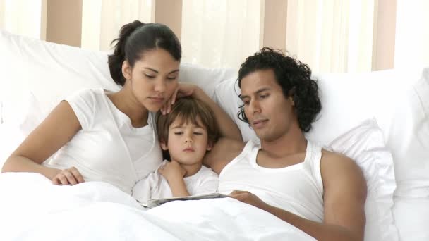 Joven familia leyendo en la cama — Vídeo de stock