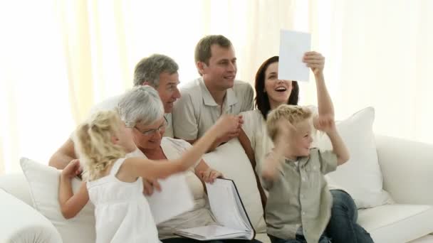 Família feliz sentada no sofá olhando para um álbum de fotos em casa — Vídeo de Stock