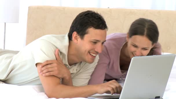 Pareja sonriente usando un portátil acostado en la cama — Vídeos de Stock