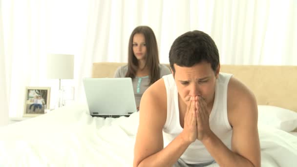 Мужчина страдает головной болью, пока его жена работает над ноутбуком — стоковое видео