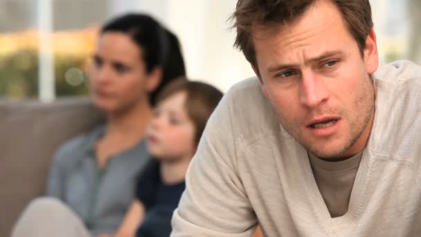 Ein Mann macht sich Sorgen, während seine Familie auf dem Sofa liegt — Stockvideo