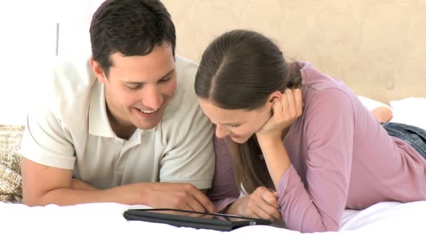 Lachende paar met behulp van een tablet-computer terwijl er liggen — Stockvideo