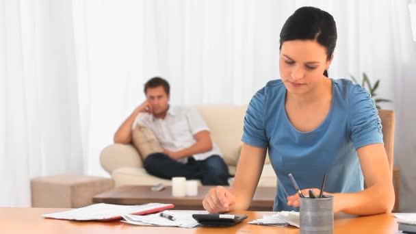 Women calculating her bills while her husband is on the sofa — Stock Video