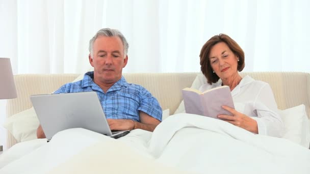 Elderly man working on his computer while his wife is reading — Stock Video