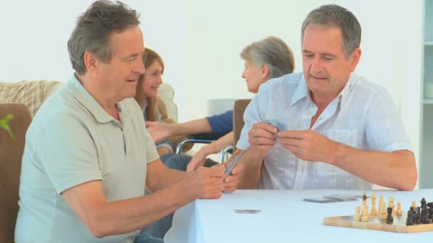 Mature friends playing cards while their wives are talking — Stock Video