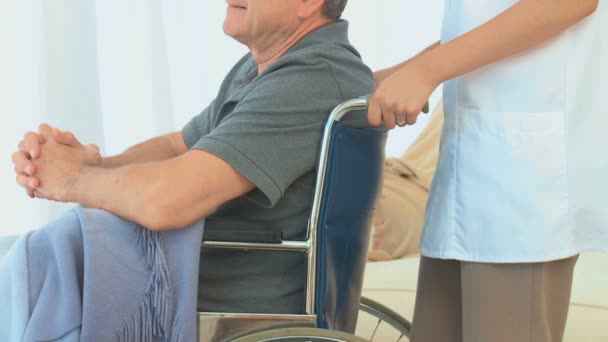 Hombre en silla de ruedas escuchando a su enfermera asiática — Vídeo de stock