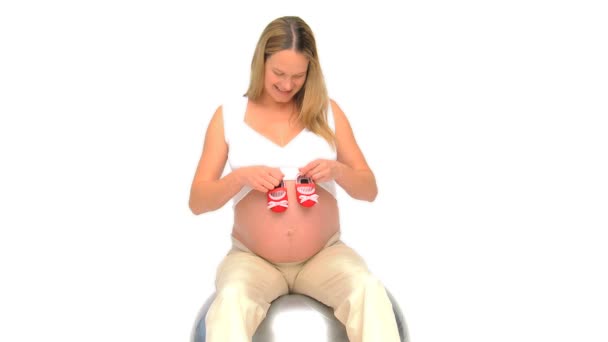 Woman on a gym ball playing with red little shoes — Stock Video
