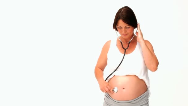 Brunette pregnant woman listening to her belly with a stethoscope — Stock Video