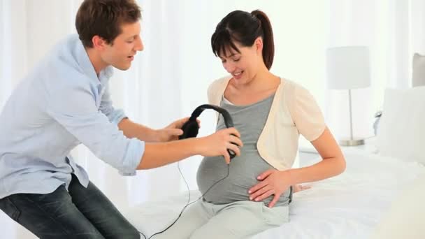 Man putting headphones on the belly of his pregnant wife — Stock Video