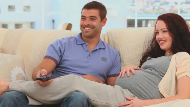Beautiful future parents watching the tv in their couch — Stock Video