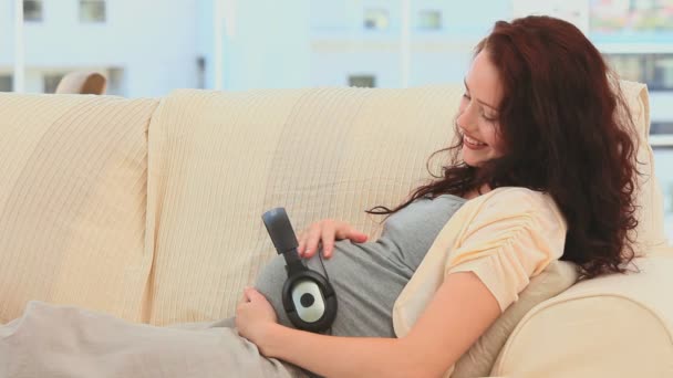 Pregnant woman with headphones on her belly — Stock Video