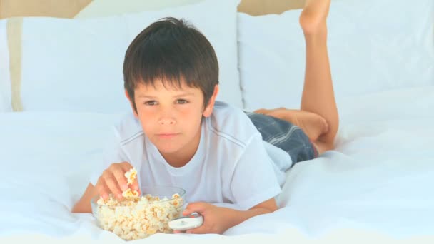 Ein kleiner Junge isst Popcorn vor dem Fernseher — Stockvideo