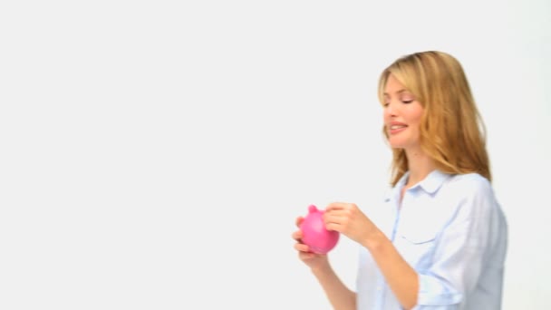 Casual blonde woman saving up money in a piggy bank — Stock Video