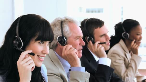 Fröhliche Callcenter-Agenten sitzen mit Headsets — Stockvideo