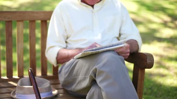 Un hombre retirado con un periódico sentado en un banco — Vídeos de Stock