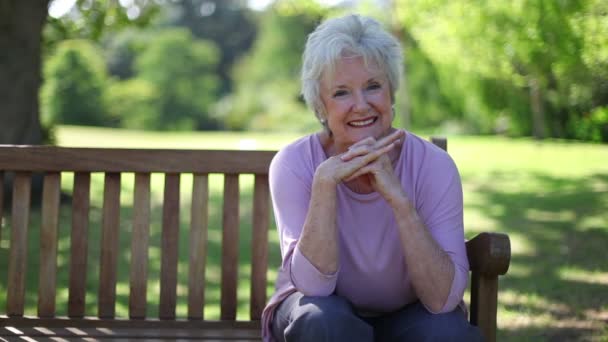 Mujer jubilada sonriendo sentada en un banco — Vídeo de stock