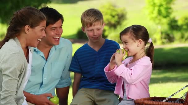 Little girl eating a green apple in front of her family — Wideo stockowe