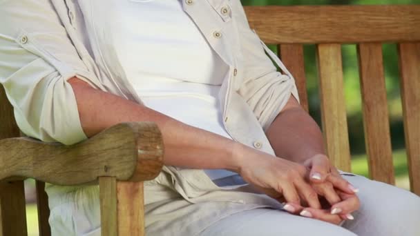 Femme mûre souriante assise sur un banc en bois — Video