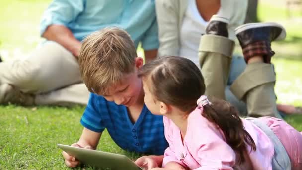 Hermanos sonrientes usando un ebook mientras mienten — Vídeos de Stock