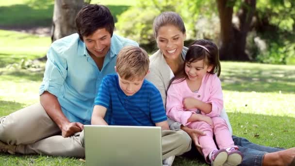 Famiglia sorridente seduta sull'erba con un computer portatile — Video Stock