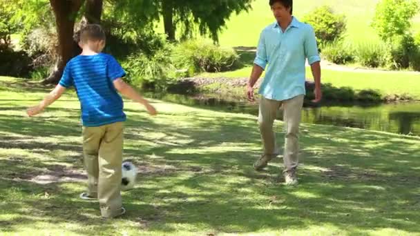 Улыбающийся мужчина играет в футбол со своим сыном — стоковое видео