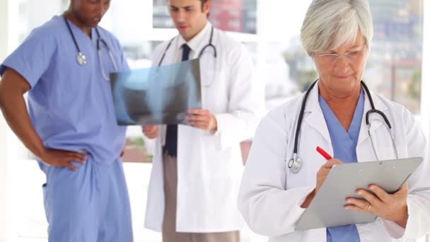 Серьёзный врач пишет на планшете перед своей командой — стоковое видео