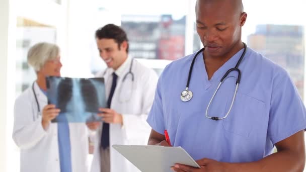 Enfermera escribiendo en un portapapeles delante de los médicos — Vídeo de stock