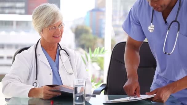 Smiling mature doctor showing documents to a nurse — Stock Video