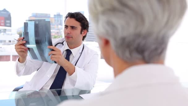 Médico sonriente sosteniendo una radiografía frente a su paciente — Vídeos de Stock