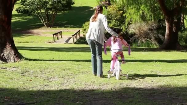 Вид ззаду жінки, яка допомагає доньці їздити на велосипеді — стокове відео