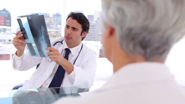 Allvarliga läkare innehar en röntgenbild framför sin patient — Stockvideo