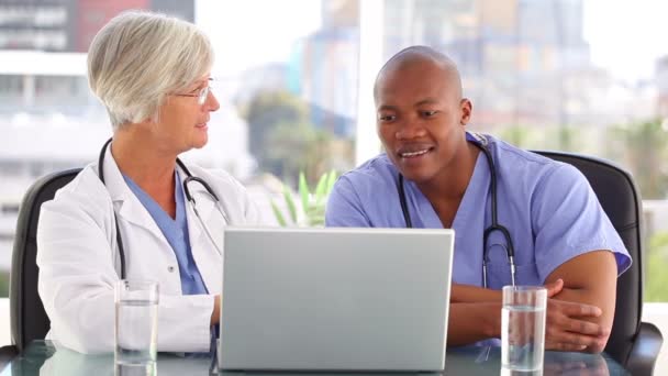 Médico sonriente hablando con una enfermera delante de un portátil — Vídeos de Stock