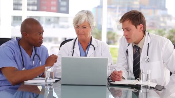 Smiling mature doctor sitting with colleagues in front of a laptop — Stock Video