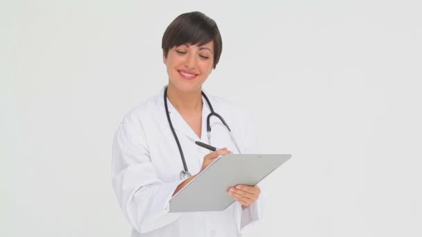 Médico sonriente escribiendo en un portapapeles — Vídeos de Stock