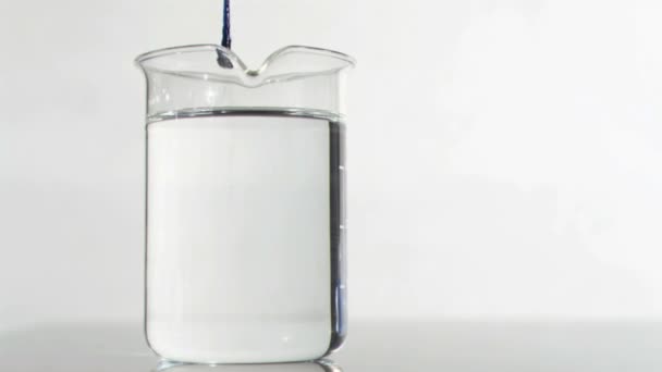 Dünnes blaues Rinnsal in Superzeitlupe, das in einem Wasser auf einem Becherglas fließt — Stockvideo