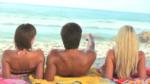 Three friends sit on their towels on the sand — Stock Video