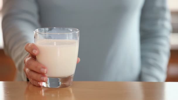 Женщина поднимает стакан молока со стола — стоковое видео