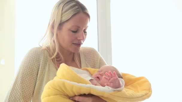 Woman smiling while holding a child in a yellow blanket — Stock Video