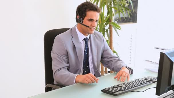 El hombre en su escritorio hablando en sus auriculares — Vídeo de stock